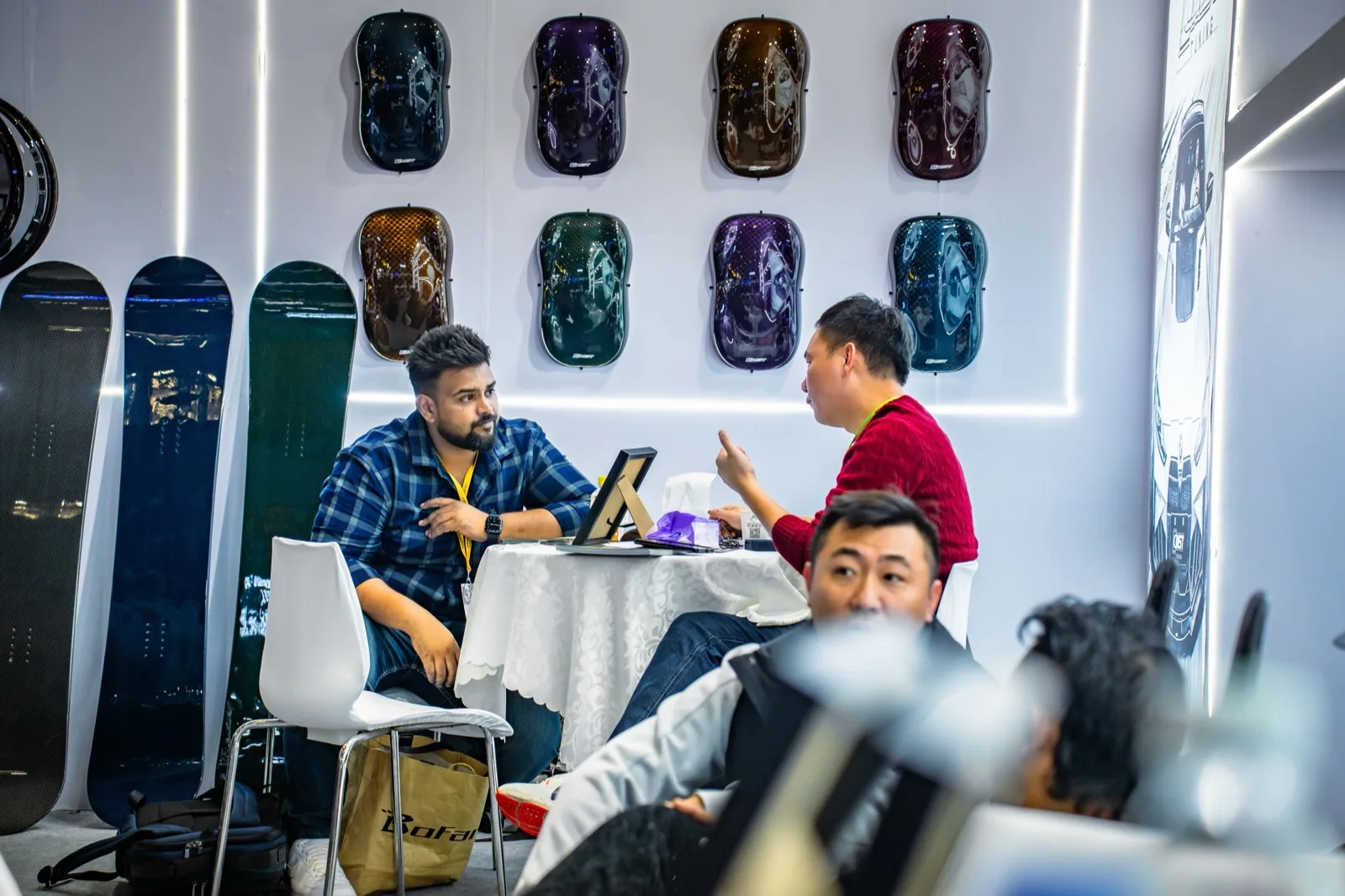 Two people talking at a table on the CMST stand, in front of a wall of carbon mirror-cap samples